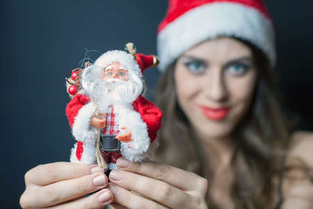 Sexy woman dressed in Santa Claus clothes gives you a toy of Santa. Black backgroundの写真素材