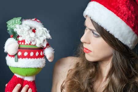 Displeased frown woman dressed in red hat looking at Santa Claus gift toy. の写真素材