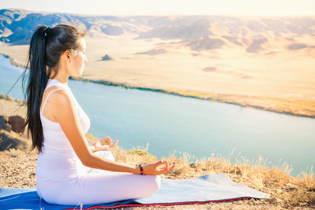 Beautiful asian woman relaxing and meditating outdoor at mountain above Ili river at China. She sits at peak of mountain in lotus position and feel harmony of your body and nature. Healthy lifestyles concept of body and soulの写真素材