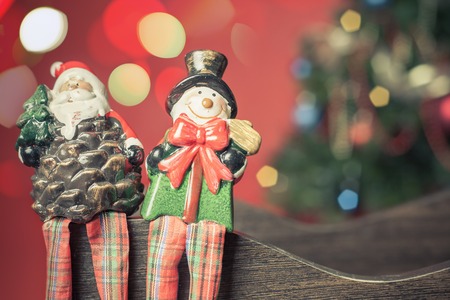 Christmas toy of Santa Claus and snowman sitting together on the eve of Christmas. On the red background is beautifully decorated Christmas tree and abstract defocused light bokehの写真素材