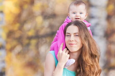 Happy child and beautiful mother outdoor at autumn park. Child is warmly dressed in a pink jacket....