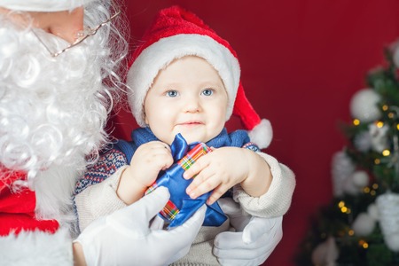 Happy baby and Santa Claus with big gift or present box! Child dressed in red Santa hat. Xmas and New Year holiday!の写真素材