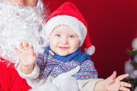 Closeup happy baby and Santa Claus waiting for gift or present. Child dressed in red Santa hat. Xmas and New Year holiday!の写真素材