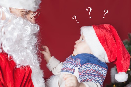 Surprised baby with question looking at Santa Claus, waiting for gift or present. Is it true that Santa Claus is real? Xmas and New Year holiday!の写真素材