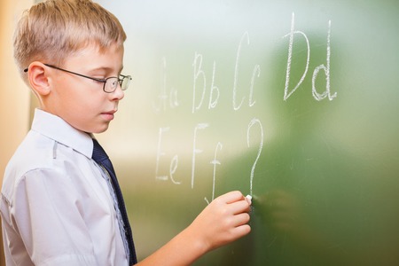 School boy writes English alphabet with chalk on a blackboard in school classroom. He does not know continuation of the alphabet and wrote a question mark.の写真素材