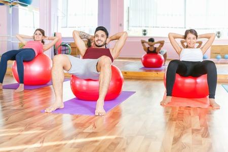 Young people lead a healthy lifestyle, exercise and engaged in fitness room. Using gimnastic ball. Flat stomach, pumping press. Exercise strengthens a person physically and make them more happy!の写真素材