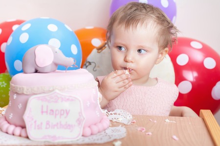 Funny baby celebrating first birthday and eating cake. Child with many balloons! Decoration at home. Make a first wish. Desireの写真素材