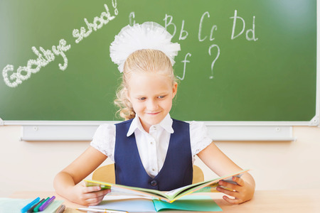 Goodbye school! Girl reading book and sitting at the desk at schoolの写真素材