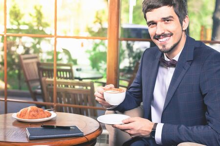 Handsome male has a french breakfast with a cap of coffee and croissant at cafe restauran. Tasty. Elegant succesful man. Smiling businesman. Mustacheの写真素材