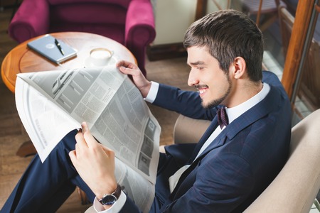 Businessman reading a newspaper at cafe, mourning. Daily news. Good news! Job searchの写真素材