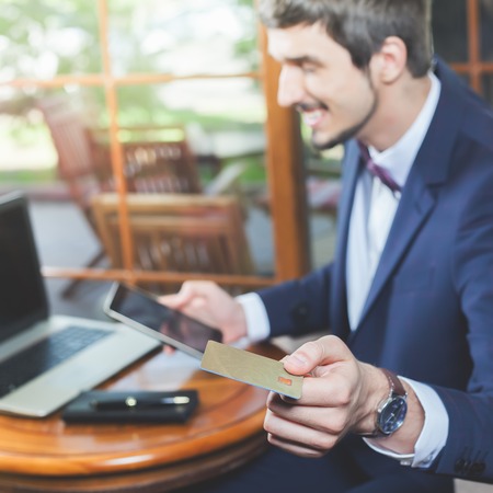 Concept of online payment by plastic card through the Internet Banking. Human hand for mobile phone and holding credit card, man pays the bill. Laptop at table. Successful businessmanの写真素材