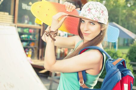 Fashion skateboarder young woman with a skateboard. Adventure at summer trip. Sport. Girl dressed in cap, wearing backpack. Accessoriesの写真素材