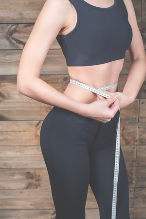 Attractive girl measure the waist, centimeters tape. Slim stomach do abdominal exercises. Workout exercise at home to lose weightの写真素材