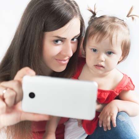 Image of funny baby and mother make selfie photo on mobile phone. Newborn looking at the camera surprised! Mothercare is most important in baby lifeの写真素材