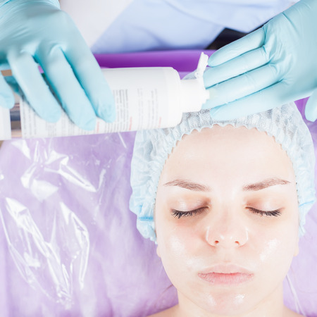 Beautiful young woman in spa salon receiving face treatment with facial cream, cotton pad. Acne. Sponge. Concept of beauty, healthy cosmetology therapyの写真素材