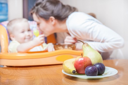 Mom feeds the baby fruits pure. Fruit. Nutrishion. Healthy and natural baby food. Fruits lying on the table. Baby food. Healthy eat. Fresh fruit, banana, apple, prune, pearの写真素材