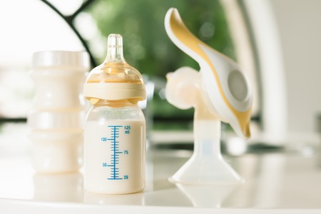 Baby bottle with milk and manual breast pump. A lot of full bottles with breast milk on the background. Mother's milk - the most healthy food for newbornの写真素材