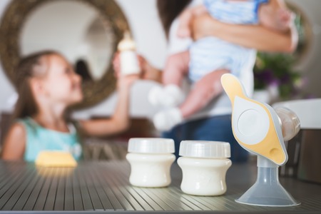 Bottle with milk and manual breast pump. Daughter holding baby bottle and helps to mother at...