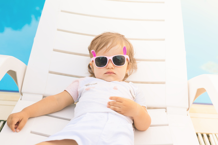 Endless summer! Cute baby relaxing at sunbed near pool at resort. A little girl wearing sunglasses. Fashion child burnの写真素材