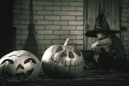 Little baby witch making a magic potion at Halloween night. Retro revival image. Horror. Pumpkins, broom. Halloween costumes for child. Witch.の写真素材