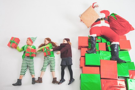 Santa's helpers are working at North Pole, elves and kids holding gift boxes. Merry Christmas. Santa sitting at many gift boxes and reading wishes list. Letters To Santa Claus. Wish list. Black Fridayの写真素材