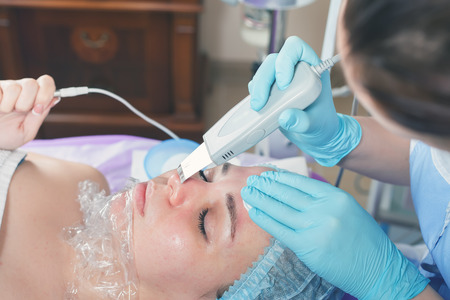 Woman in spa salon receive skin treatment. Facial rejuvenation. Ultrasonic cleaning of the face. Creating occlusion for better atomization of the upper layer of the skin.の写真素材