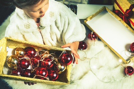 Cute toddler girl decorating a Christmas tree. Red balls. New Year 2017. Fairy tale. Dressed in...
