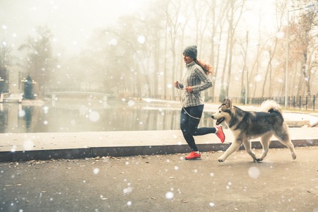 Image of young girl running with her dog, alaskan malamute, outdoor at autumn or winter. Mourning jogging. Domestic pet. Husky. Guide-dogの写真素材