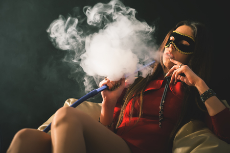 Young, beautiful girl with carnival mask smoke a hookah