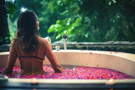 Woman relaxing bath with tropical flowers outdoor at luxury hotelの写真素材