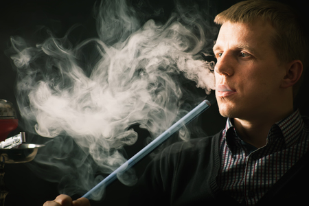 Closeup Young, handsome man smoke a hookah at clubの写真素材