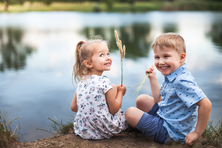 Your Happy Kids, Girl And Boy Are Sitting Near Lakeの写真素材
