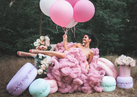 Fashion sexy woman dressed in pink stunning dress surrounded of French Macaronsの写真素材