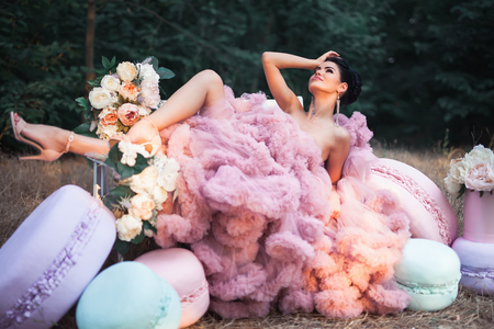 Fashion sexy woman dressed in pink stunning dress surrounded of French Macaronsの写真素材