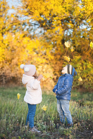 Happy kids walking outdoor at autumn park throw leavesの写真素材