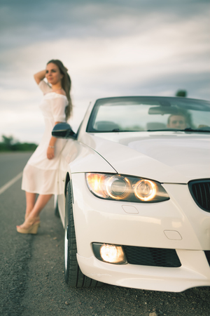 Young woman with white dress standing at the white carの写真素材
