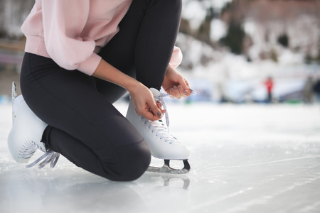 Woman tie shoelaces figure skates at ice rink close-upの写真素材