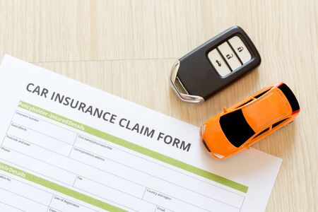 Top view of car insurance claim form with car key and car toy on wooden deskの写真素材