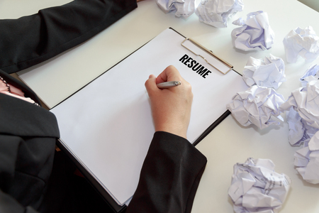 Hands of female writing resume with crumple sheets of papers at the office desk.