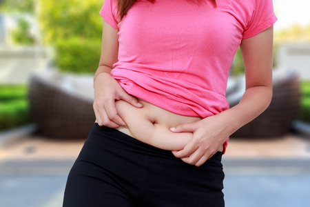 Chubby woman hand holding her own belly fat.の写真素材