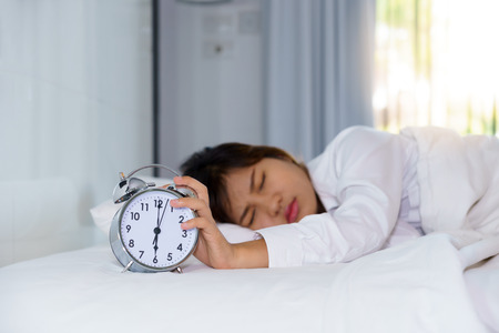 Sleepy young woman stretching hand to trying kill alarm clock in the morning. early wake up.の写真素材