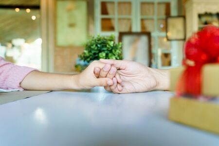 A couple holding hands each other in restaurant with a golden gift box with red ribbonの写真素材