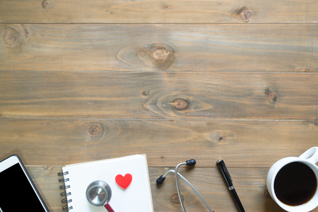 Top view of blank notepad on wooden desk with smartphone, pen, stethoscopes and coffee cupの写真素材