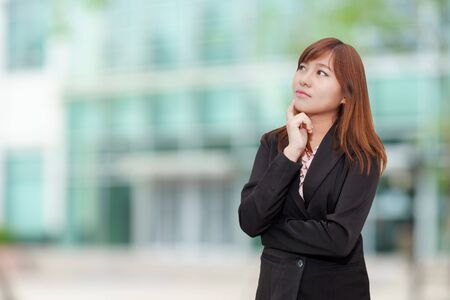 Business woman in black suit thinking in front of buildingの写真素材