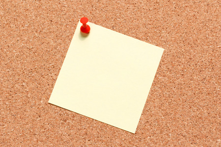 Blank yellow sticky notes on cork board with red pin