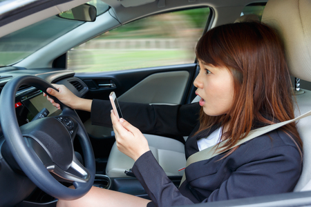 Shocked woman watching video or text to someone with smart phone while driving fast a car distracted.の写真素材