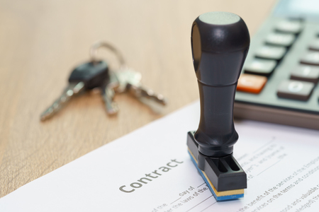 Contract document with approved rubber stamp and key on wooden deskの写真素材
