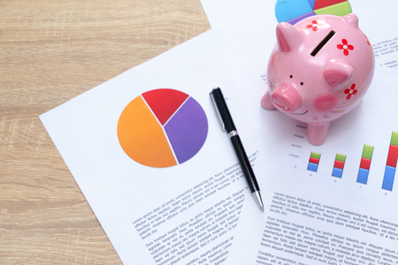 Pink piggy bank with graph and pen on wooden desk - growing interest rate conceptの写真素材