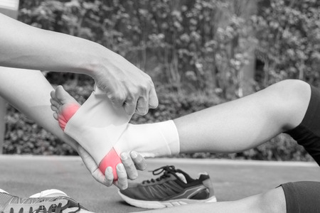 Young woman runner ankle being applied bandage by man in park. injury ankle - black and white...