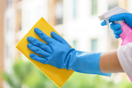 Hands of housekeeper cleaning mirror with green cloth